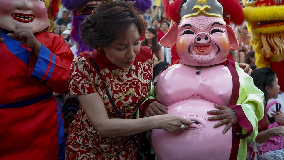 A woman puts money inside the belly bottom of a performer in pig costume during a performance to celebrate the Lunar New Year, or Spring Festival, in Chinatown