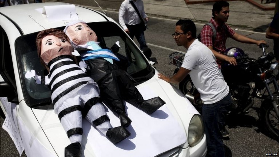 Водитель такси смотрит на пинаты с изображением бывшего вице-президента Роксаны Балдетти (слева) и президента Гватемалы Отто Переса Молина во время демонстрации с требованием отставки г-на Переса Молины в городе Гватемала 27 августа 2015 г.