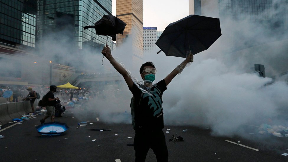 Протестующий поднимает зонтики, когда спецназ применяет слезоточивый газ для разгона протестующих у здания правительства в Гонконге (28 сентября 2014 г.)