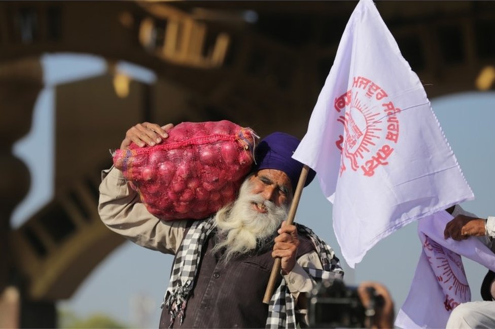 A farmer carries a bag of onions and a flag prior to the start of a march towards New Delhi to protest against new farm laws, on the outskirts of Amritsar, India, 27 November 2020.