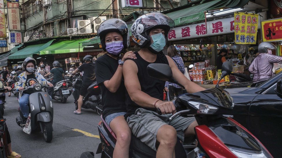 台北街頭一對男女搭乘摩托車走過市集（6/7/2022）