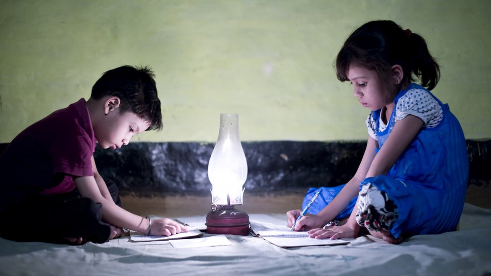 Dos niños haciendo tarea con una lámpara.