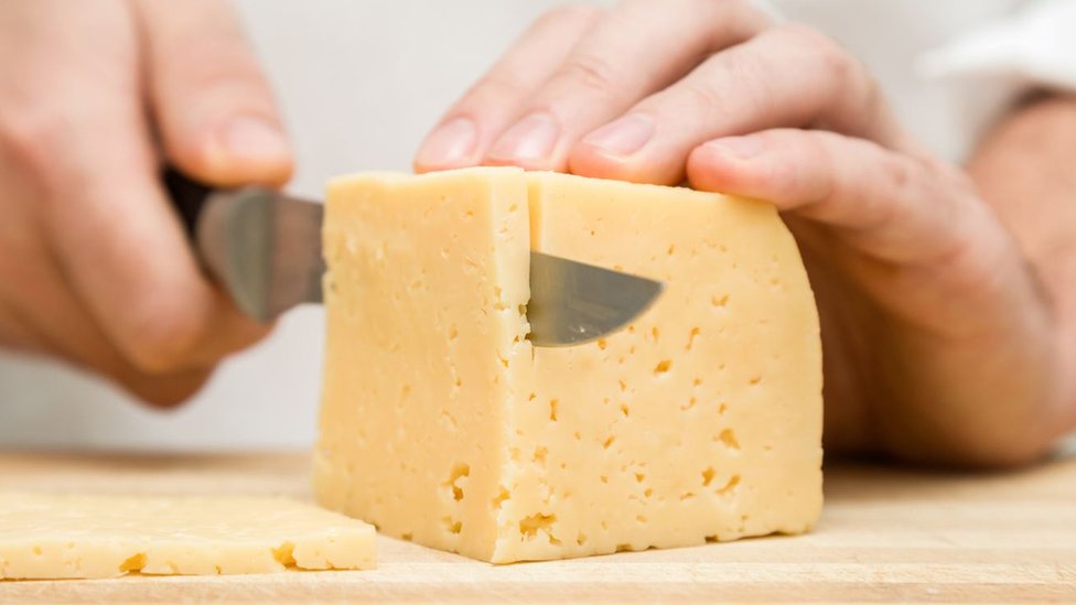 Una persona cortando un trozo de queso