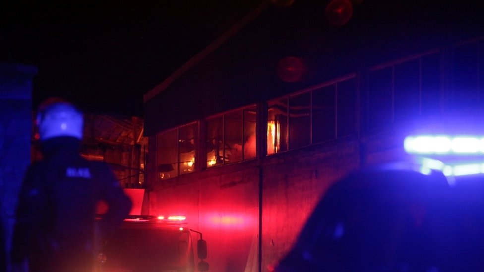 Полицейский стоит на страже у горящего помещения центра One Happy Family на острове Лесбос