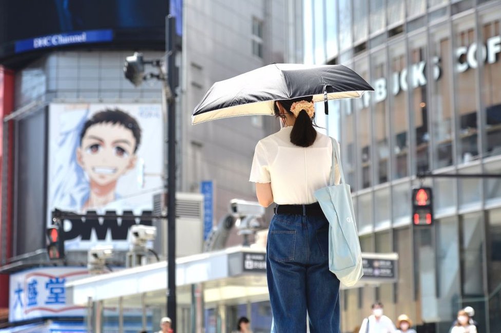 شابة تسير في الشارع تستخدم مظلة لحماية نفسها من الشمس في منتصف نهار 27 يونيو حزيران عام 2022 في حي شيبويا الشهير بطوكيو في اليابان.