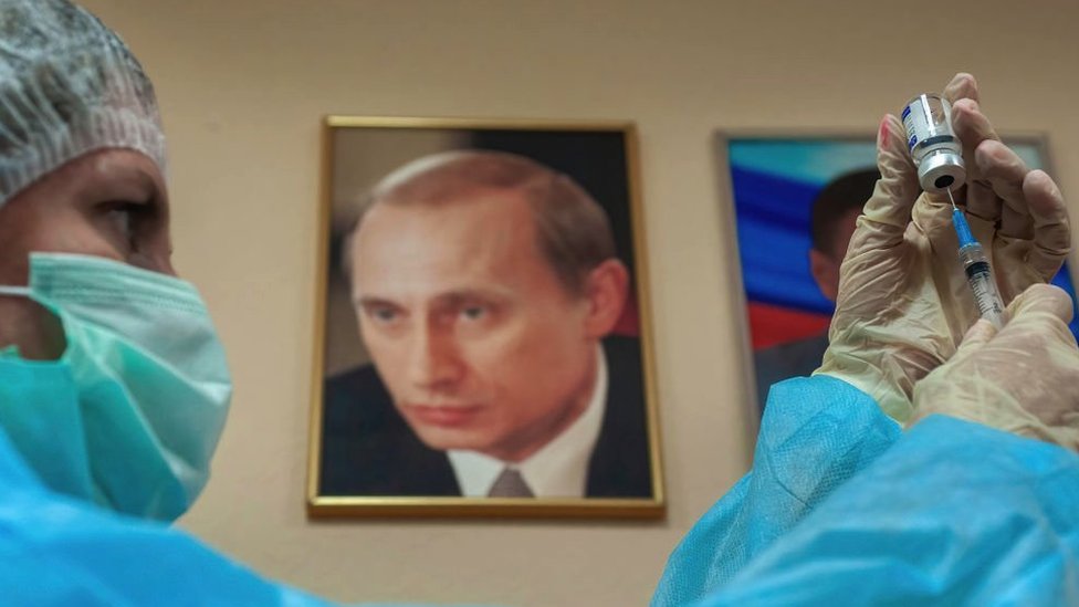 Russo com vacina e retrato de Putin ao fundo