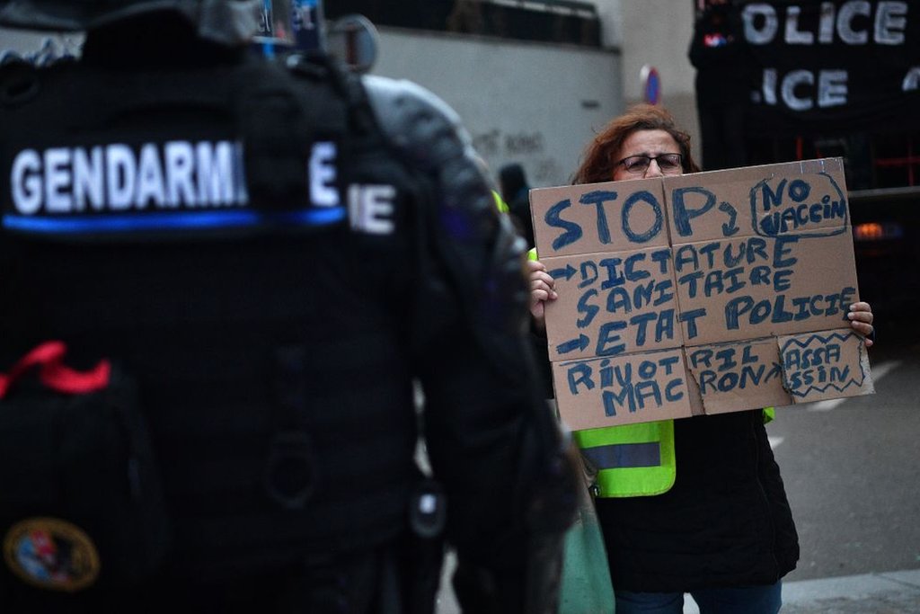 Protester holding an anti-vaccine sign in front of gendarmes.