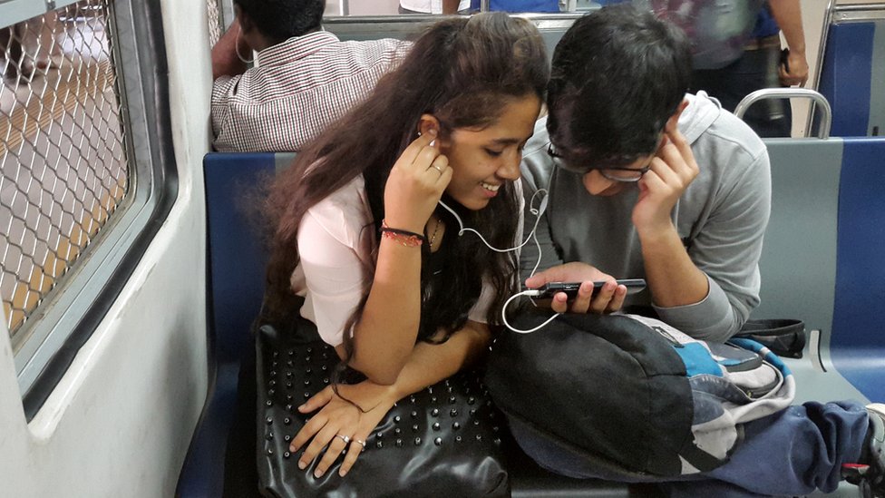 На этой фотографии, сделанной 7 марта 2017 года, показаны индийские студенты, просматривающие фильм на своих смартфонах, когда едут в пригородном поезде в Мумбаи. Выкуп, слияния и быстрые выходы - по мере того, как самый богатый человек Индии встряхивает сверхконкурентный рынок мобильной связи страны, телекоммуникационные компании изо всех сил пытаются либо консолидировать, либо сократить свои убытки и уйти.