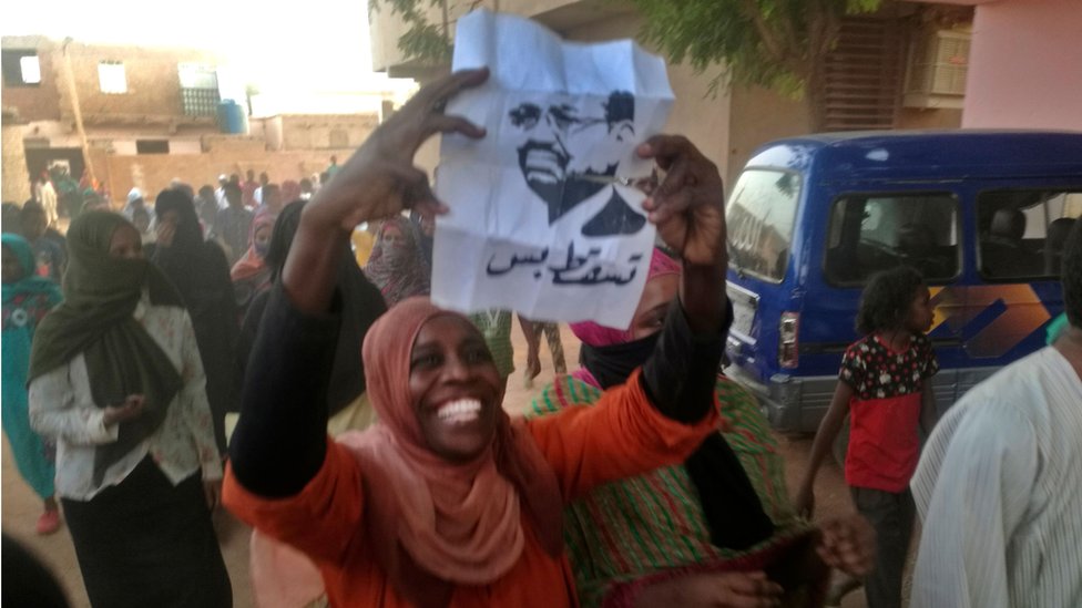 امرأة مشاركة في الاحتجاجات ضد نظام الرئيس عمر البشير في السودان ترفع صورة البشير مرفوقة بعبارة "تسقط بس"