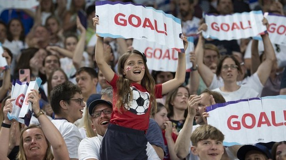 Niñas y mujeres aficionadas al fútbol sostienen carteles en los que se lee "¡Gol!", durante un encuentro de Inglaterra en la Eurocopa Femenina 2022