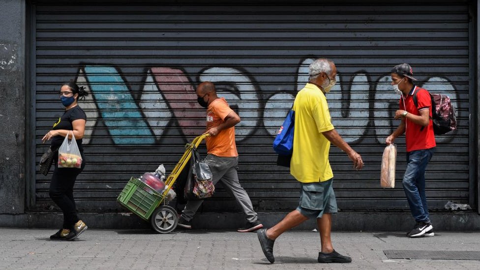 Personas caminan en una calle de Caracas con una pintada de apoyo a Nicolás Maduro.