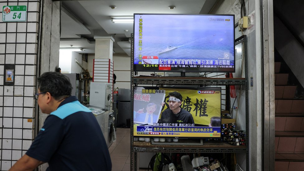 A man rides a bike past a television screen showing the news of Taiwan's Coast Guard operation after China announced military drills in areas around the island of Taiwan, in Taipei, Taiwan May 23, 2024