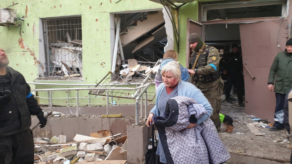 Un mujer con sangre en el rostro frente al edificio destruido de la maternidad de Mariúpol bombardeada el 9 de marzo