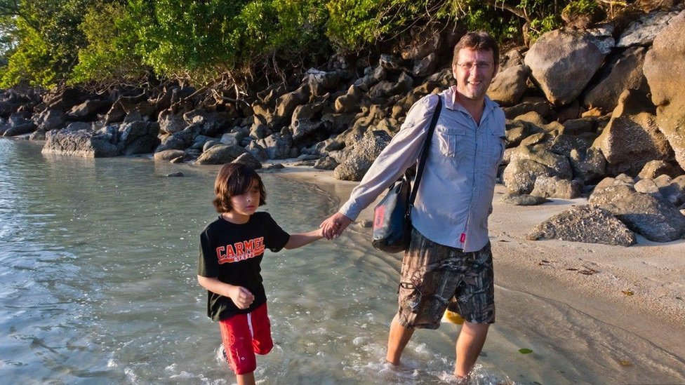Un niño de la mano con su padre caminando en el agua.