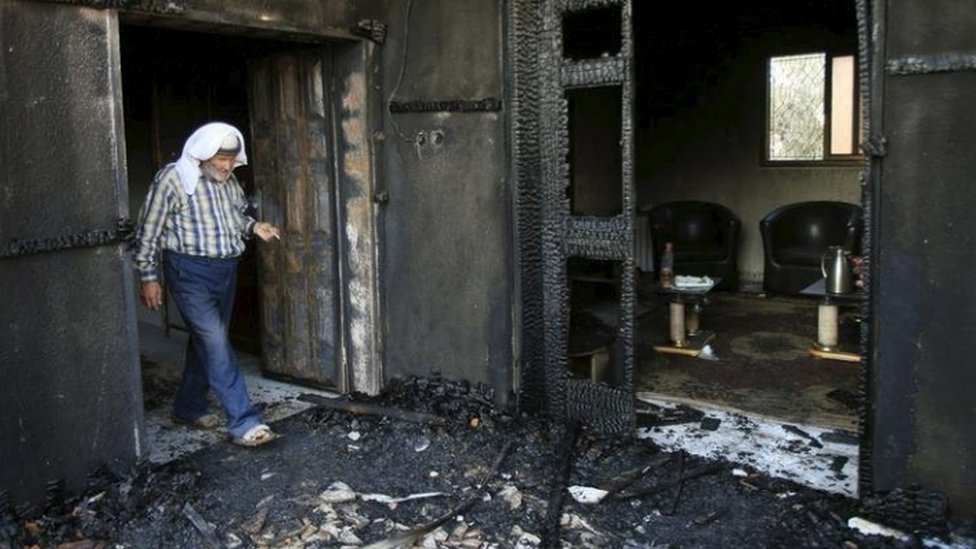 Мужчина просматривает сильно сгоревший дом палестинской семьи