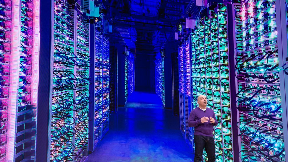 A man standing in a data centre with rows and rows of stacked server machines stretching into the distance