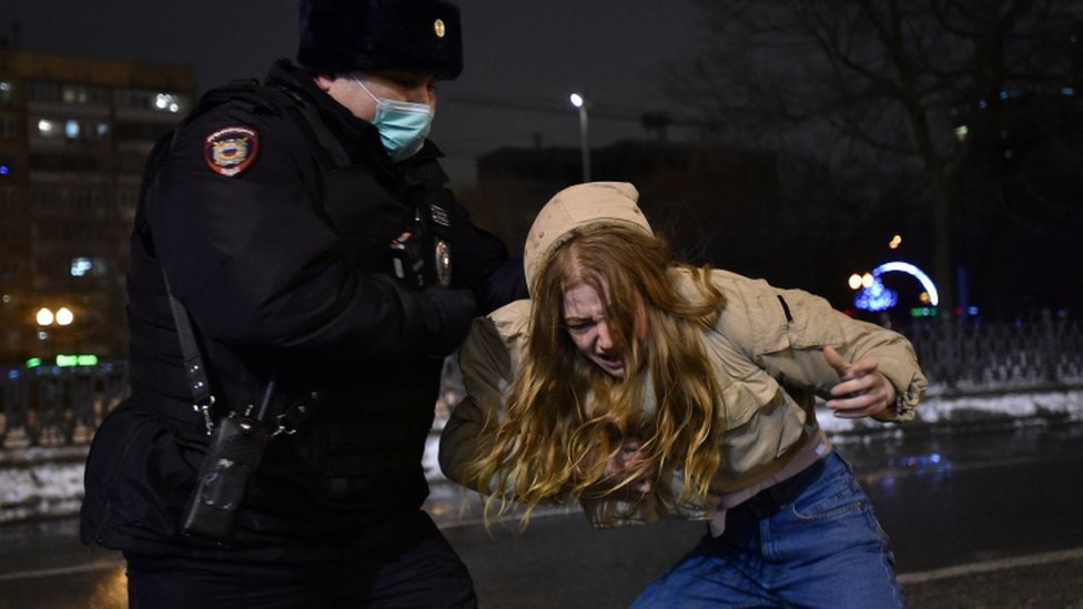 A law enforcement officer detains a woman who is bent over at Moscow protest