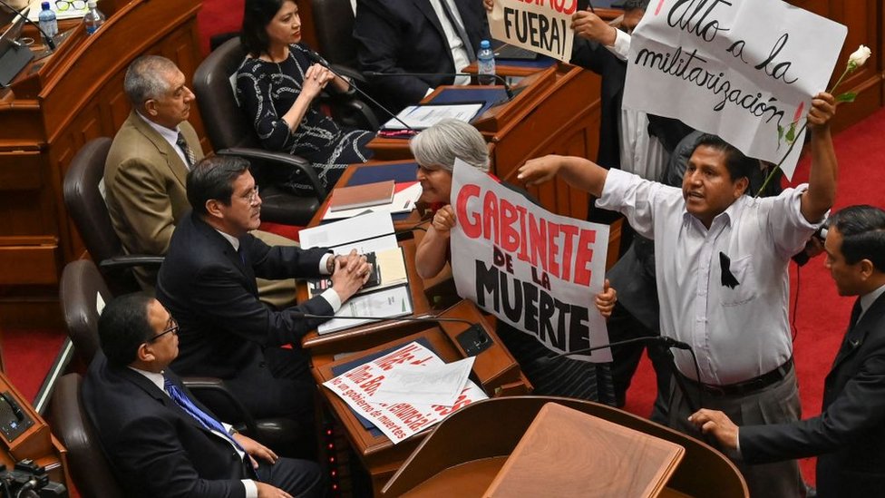 Otárola observa desde su asiento en el Congreso como diputados de oposición le muestran una pancarta con el mensaje "gabinete de la muerte".