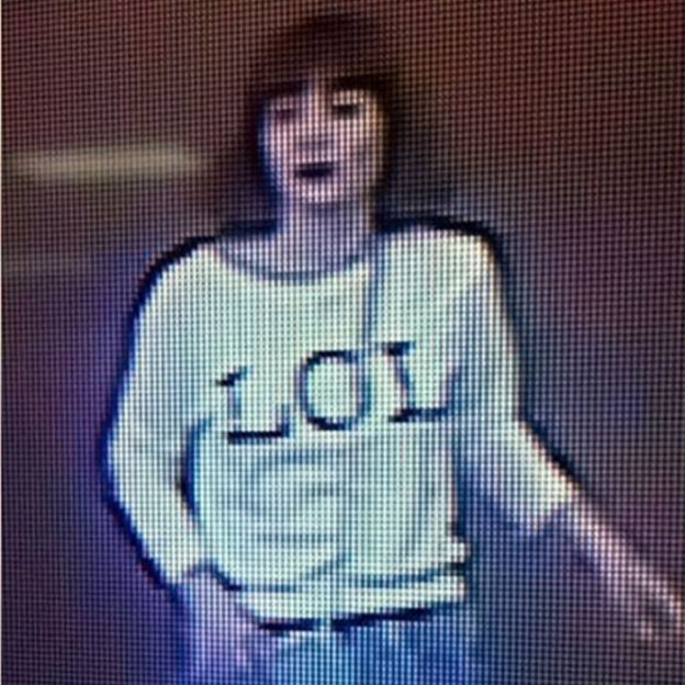 Зернистое изображение показывает женщину с каштановыми волосами в футболке с вышитыми буквами «LOL»