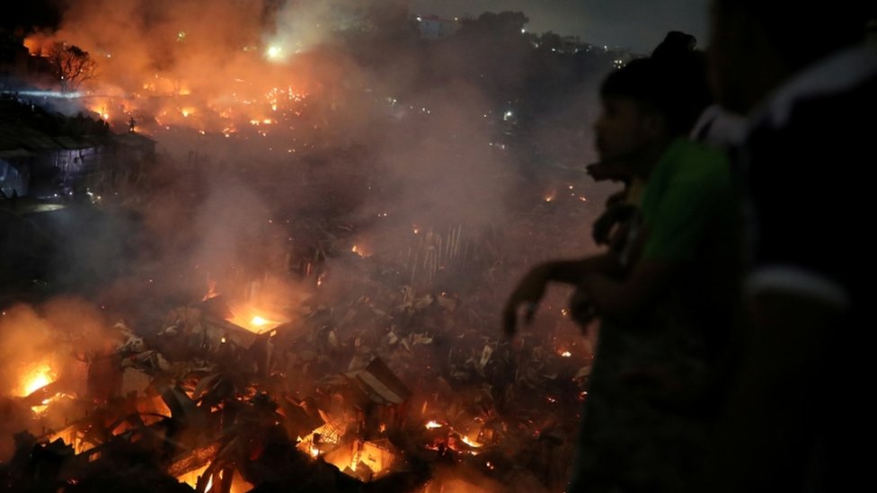 Люди собираются на крыше, чтобы посмотреть на пожар, вспыхнувший в трущобах в Дакке, 16 августа