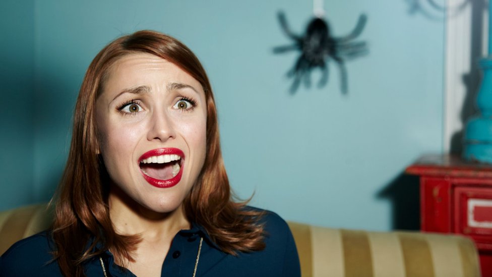 A woman scared by a spider hanging from a thread