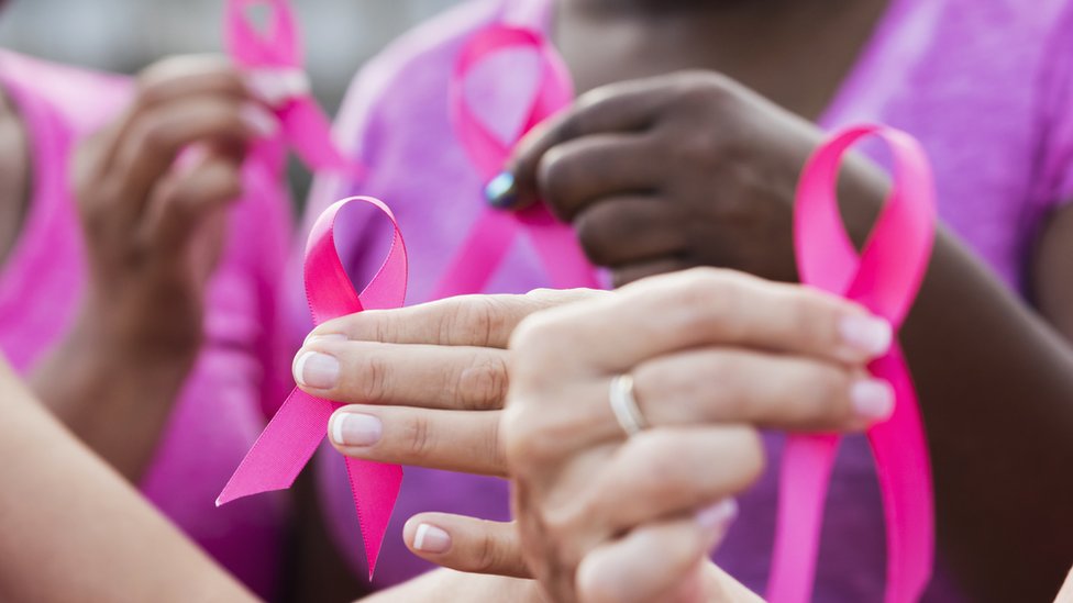 Manos con cintas rosas que reprensentan la lucha contra el cáncer de mama.