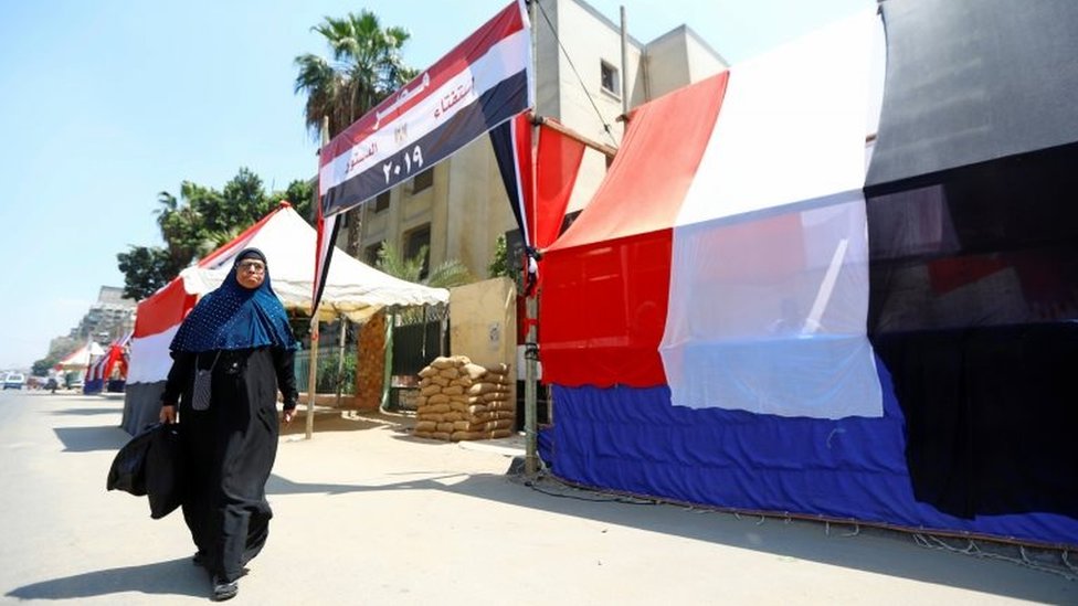 Египтянка идет перед избирательным участком, покрытым снаружи египетскими флагами, во время подготовки к предстоящему референдуму по конституционным поправкам в Каире, Египет, 18 апреля 2019 года