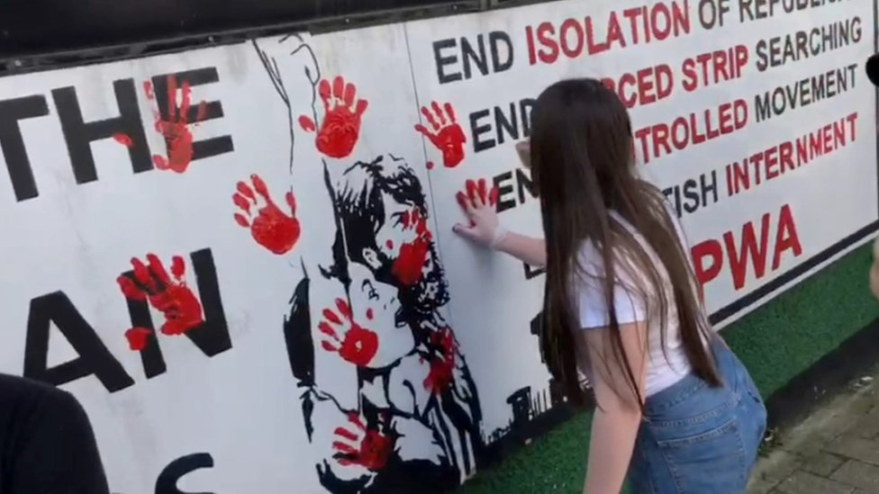 Женщина размазывает красный отпечаток руки на стене
