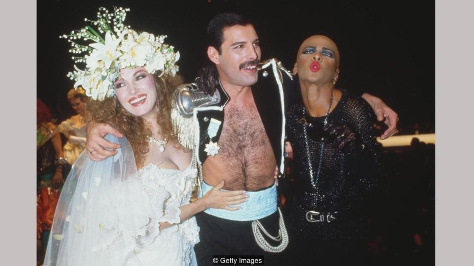 Jane Seymour dalam gaun Emanuel, bersama Freddie Mercury dan seorang teman di acara amal Fashion Aid pada 1985.