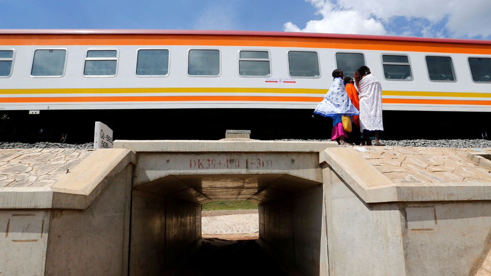 Women stand next to a train on the Standard Gauge Railway line in Kimuka, Kenya in 2019