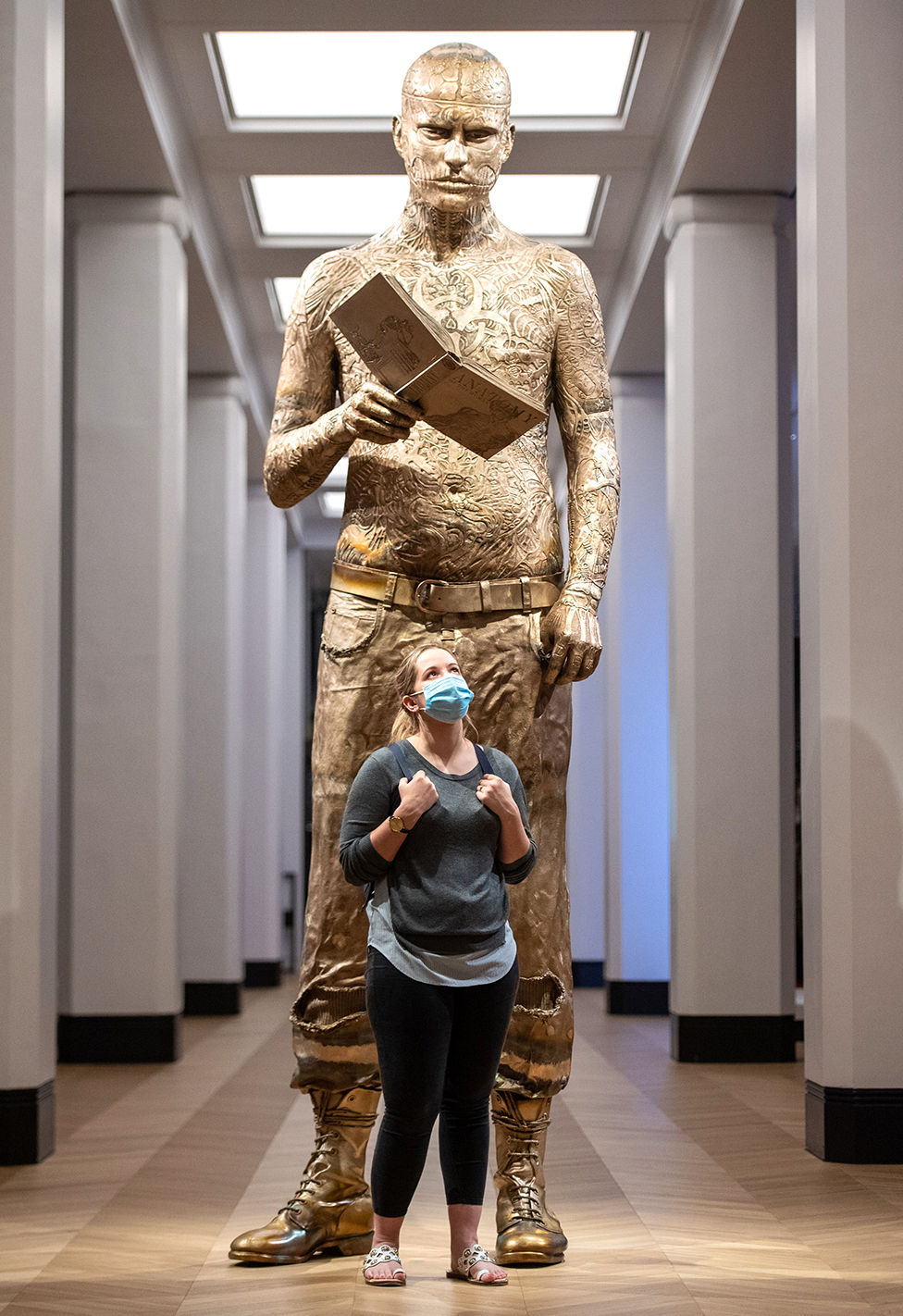 A woman stands in front of a giant statue of a tattooed man
