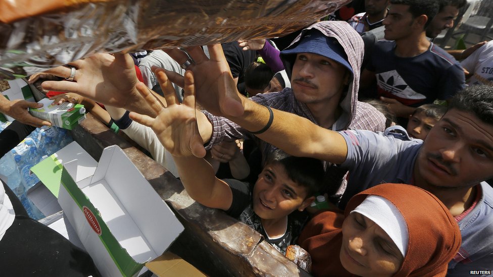 Сирийские беженцы и другие мигранты изо всех сил пытаются получить сухую пищу во время раздачи помощи работниками муниципалитета Кос на греческом острове Кос 14 августа 2015 года.