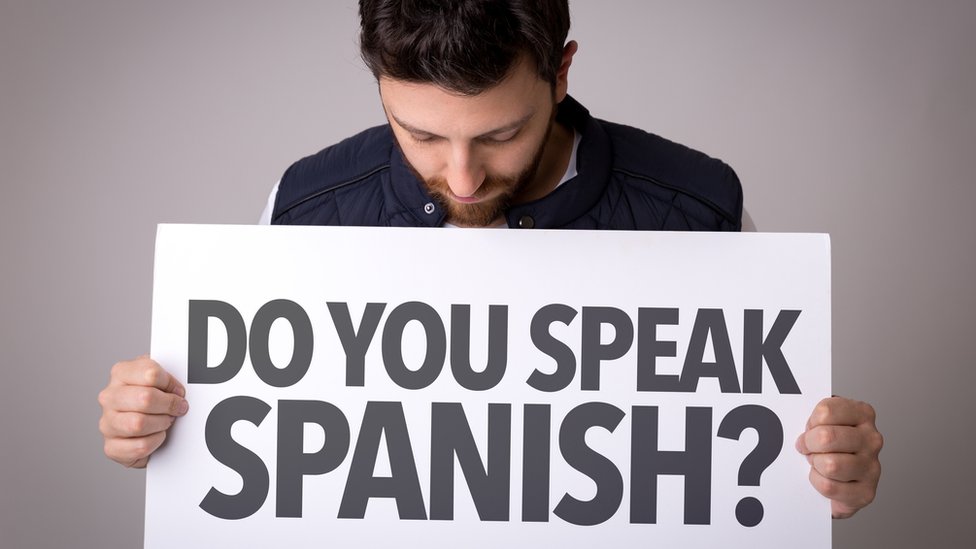 Un hombre sostiene un cartel con la pregunta en ingles: ¿Hablas español?