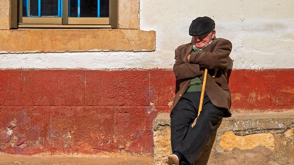 Cambiar el horario en España pondría en peligro la tradicional costumbre de la siesta. Una persona toma una siesta apoyado de una pared en la calle