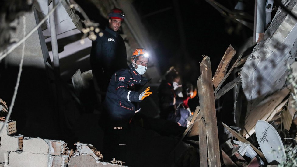 Rescue workers walking through a collapsed building at night.