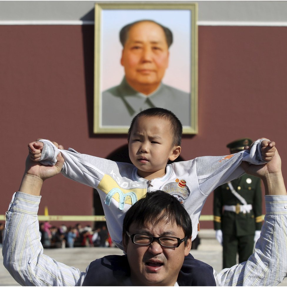 Мальчик сидит на плечах своего отца, когда они позируют фотографу перед гигантским портретом покойного председателя Китая Мао Цзэдуна на воротах Тяньаньмэнь в Пекине, Китай, октябрь 2011 года.