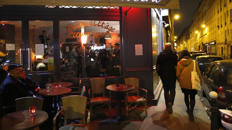 Два человека идут по дорожке возле ресторана, а еще двое сидят на сиденьях снаружи кафе / ресторана в Париже