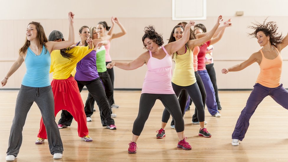 Группа женщин тренируется и танцует во время занятия в тренажерном зале.