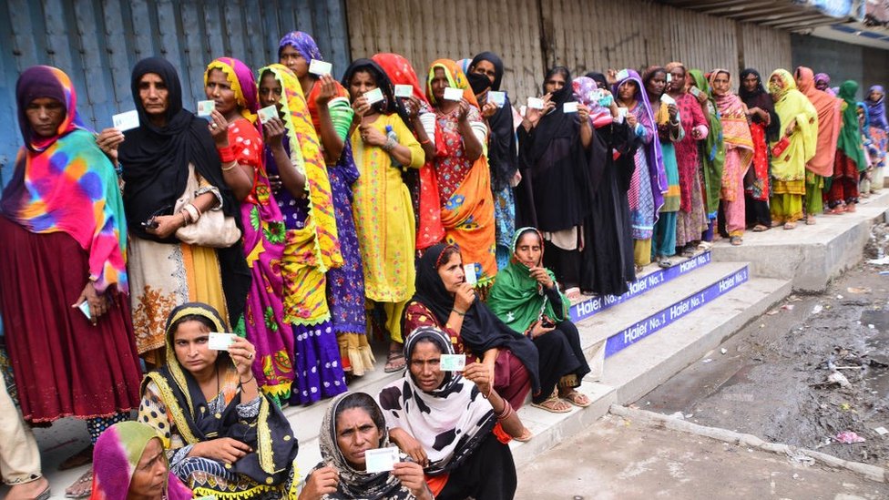 Una cola enorme de mujeres vestidas con saris coloridos hace cola a la espera de ayuda económica.