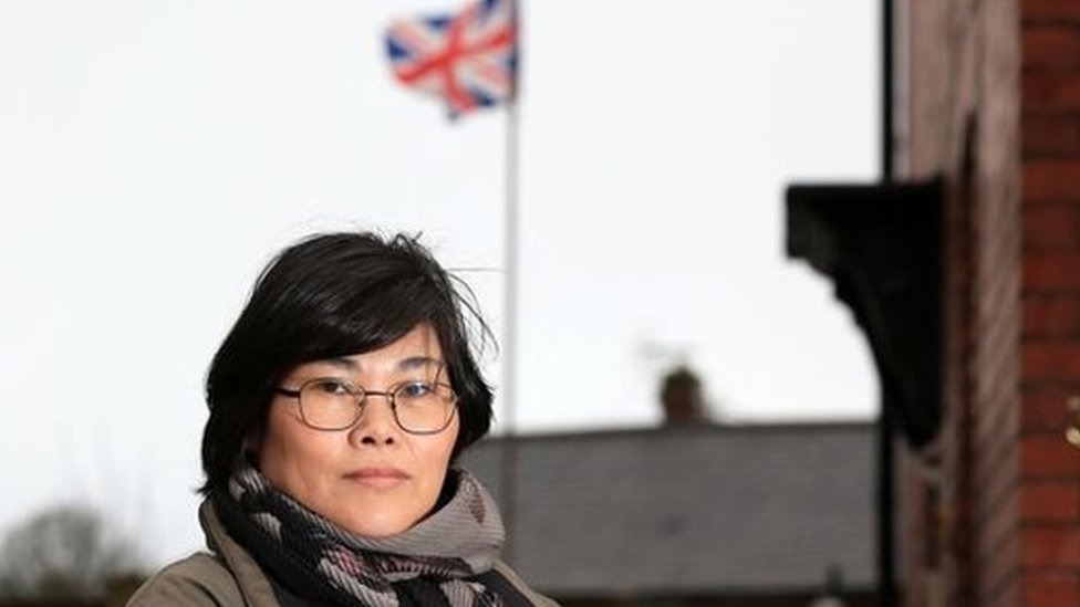 Jihyun Park berdiri di depan sebuah rumah dengan bendera Britania Raya berkibar di belakang