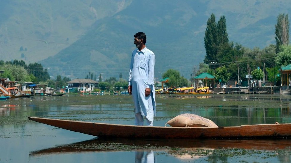 Индийский кашмирский мужчина стоит в традиционной лодке, известной как Shikara whiel, путешествуя по озеру Дал в Сринагаре 18 августа 2019 г.