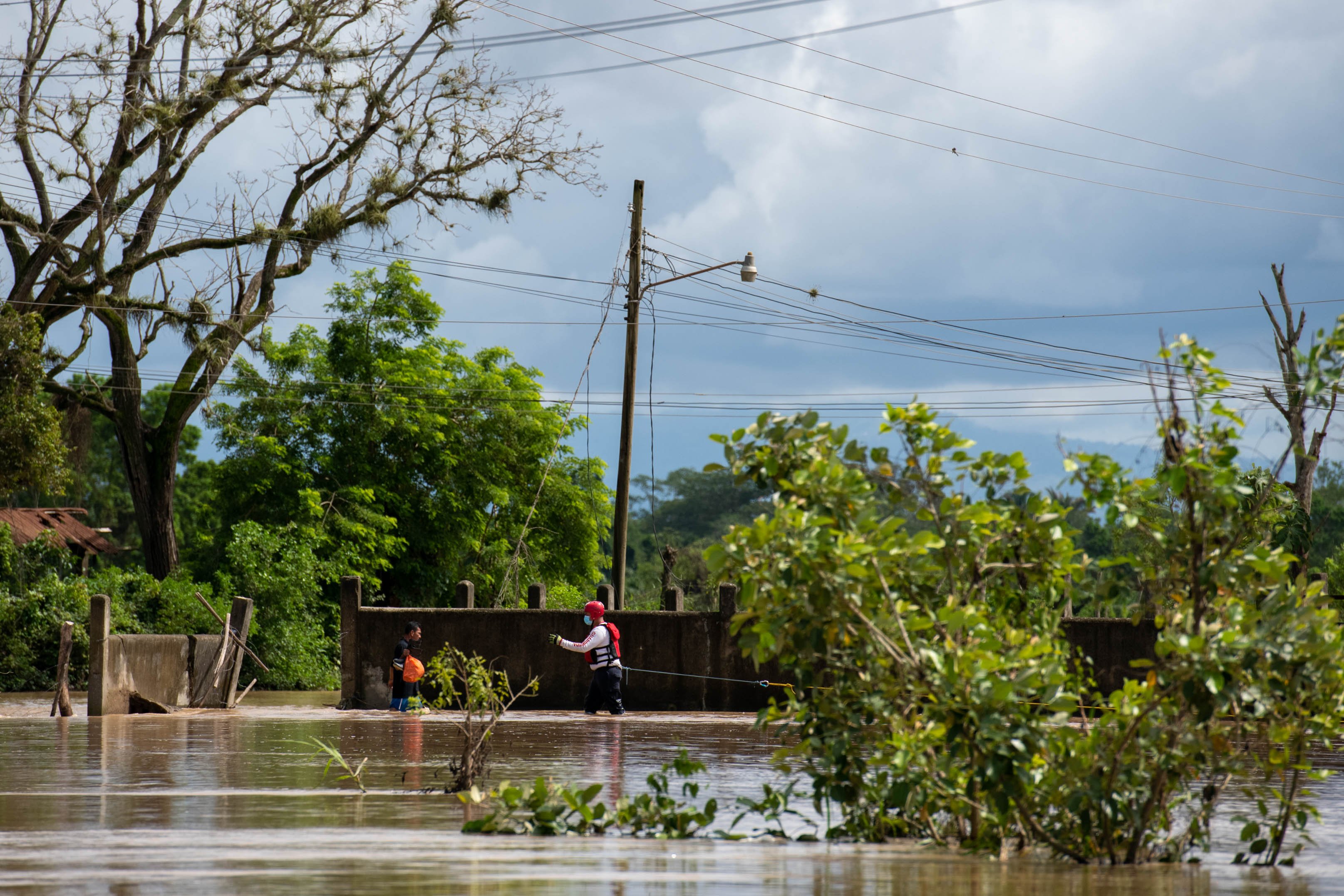 .Хуан Аргуета стоит в водах наводнения, когда к нему приближается спасатель из Красного Креста
