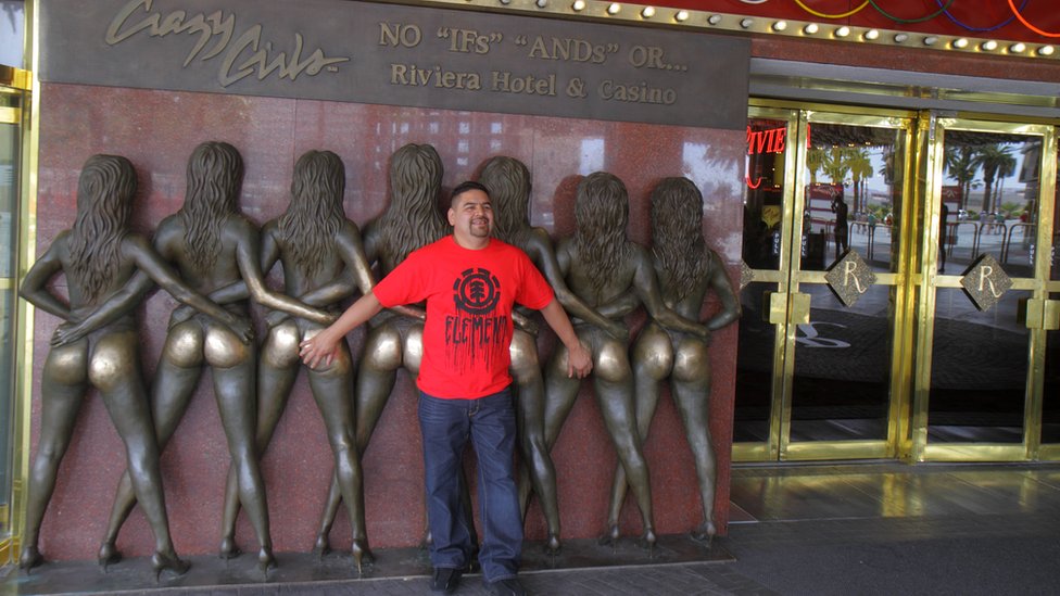 Muškarac pozira sa bronzanim statuama golišavih devojaka