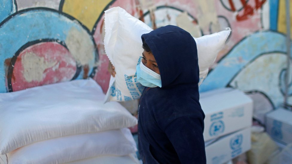 طفل فلسطيني يحمل كيس طحين من المساعدات في غزة