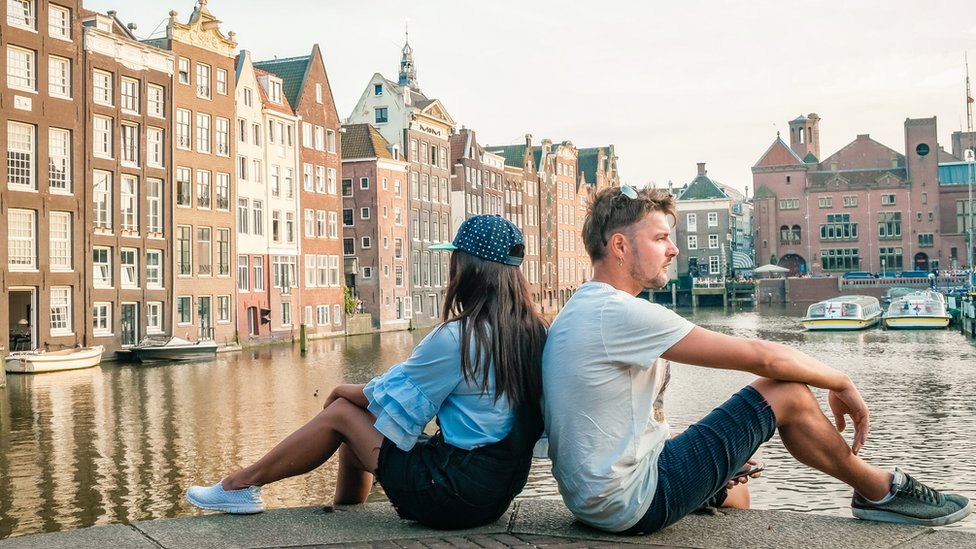Dos personas dándose la espalda sentados en un canal de Ámsterdam.