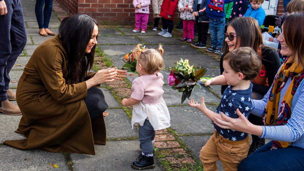 The Duchess of Sussex crouches down to greet a toddler outside Windsor's Broom Farm Community Centre