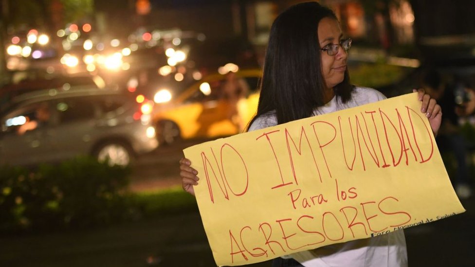 Una mujer protesta en El Salvador con una pancarta que dice "No impunidad para los agresores".