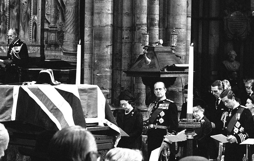 El ataúd de Lord Mountbatten cubierto con la bandera descansa sobre un catafalco durante el funeral en la Abadía de Westminster. De izquierda a derecha: la reina Isabel II, su esposo, el duque de Edimburgo, la reina Isabel, la reina madre y el príncipe de Gales, 5 de septiembre de 1979.