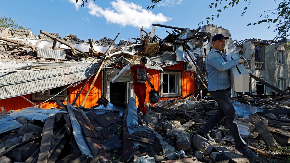 Dos hombres intentan limpiar escombros de una casa destruida en Luhansk