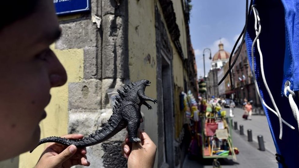 Поклонник держит пластиковую игрушку Годзилла во время просмотра съемок сцен из фильма «Годзилла, король монстров» в историческом центре Мехико 20 августа 2017 года.